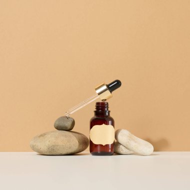 Kahverengi cam bir şişe, pipetli ve kahverengi etiketli bir taş üzerinde duruyor. Kozmetik için konteyner