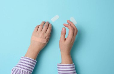 Kadın eli ve kahverengi tıbbi yapıştırıcı cilt yaralanmaları ve kesiklerin tedavisi için, mavi arka plan