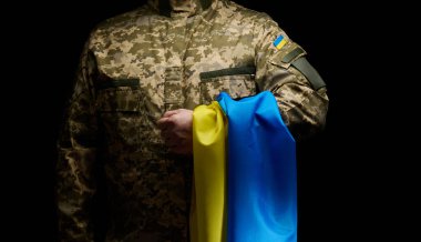 a soldier of the Ukrainian armed forces stands with a blue-yellow flag of Ukraine on a black background. Honoring veterans and commemorating those killed in the war
