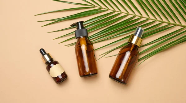 Kahverengi arka planda pipeti, spreyi ve spreyi olan cam kahverengi kozmetik şişeleri. Sıvı ürünler için kaplar
