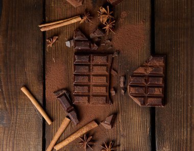 Koyu çikolata parçacıkları, tarçın çubukları ve kahverengi ahşap bir masada yıldız anason.