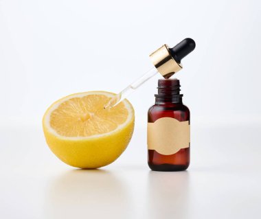 Üzerinde boş bir kağıt etiket ve pipet olan kahverengi cam bir şişe, yanında beyaz bir önü yarım limon. Kozmetikte meyve asitleri