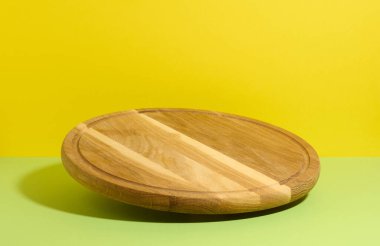 Sarı arka planda yuvarlak ahşap mutfak pizza tahtası, çatallar havada asılı.