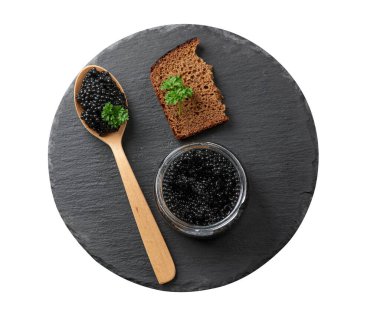 Tahta kaşıkta siyah havyar, bir dilim ekmek ve siyah yuvarlak grafit tahtada bir kavanoz.