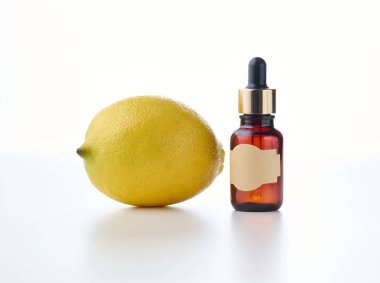 Pipetli kahverengi cam şişe ve boş bir kağıt etiket, limon. Beyaz arkaplanda doğal kozmetik ürünler