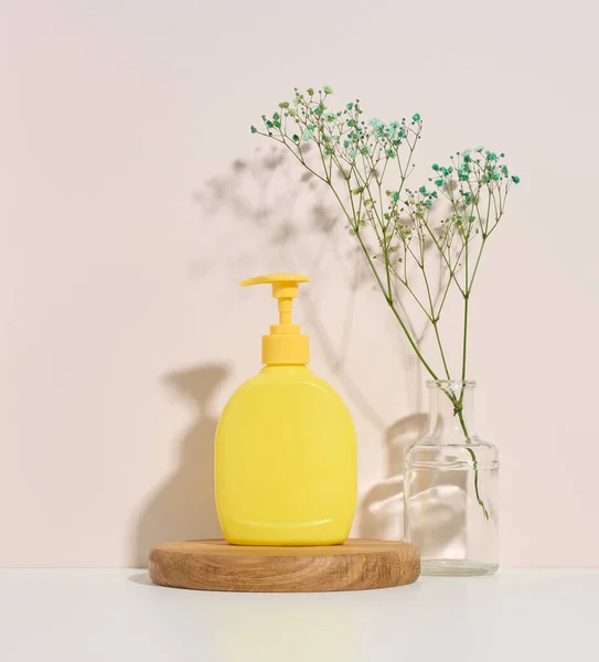 yellow plastic container with a dispenser on a wooden background and palm branch on a beige background. Container for liquid soap, shampoo