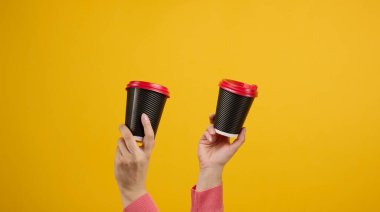 El, kahve için karton kahve bardağı tutuyor, sarı arka plan. Çevre dostu sofra takımı