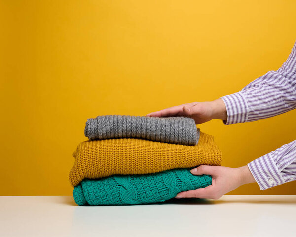 a woman holds a stack of washed folded things on a yellow background. Home routine work