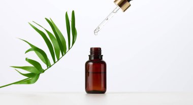 Kehribar cam damlacıktan dökülen temel yağ. Mavi bir şişe kozmetik yağı, pipetli, beyaz arka plan.