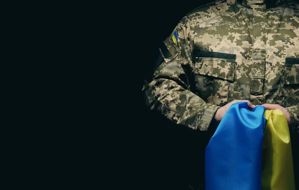 Ukrayna silahlı kuvvetlerinin askeri siyah bir arka planda mavi-sarı Ukrayna bayrağıyla duruyor. Gazileri onurlandırmak ve savaşta ölenleri anmak. Boşluğu kopyala