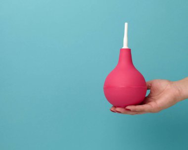 Mavi eldivenli bir el mavi arka planda pembe kauçuk lavman tutar, boşluğu kopyala