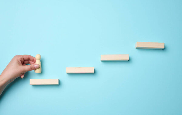 wooden steps and a figurine of a little man in a woman's hand. Startup, starting a new successful business, achieving goals