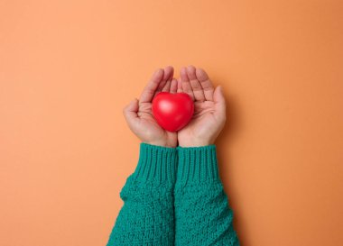 Kadın eli kırmızı kalp, turuncu arka plan. Aşk ve bağış konsepti