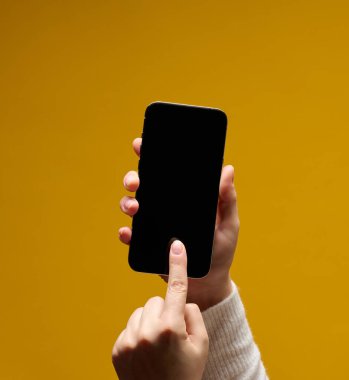 Sarı arka planda boş siyah ekranlı akıllı telefonu tutan kadın.