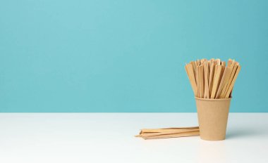 Tek kullanımlık kağıt bardaklar ve tahta çubuklar beyaz masada, mavi arkaplan, kopyalama alanı