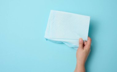 Kadın eli mavi arka planda tek kullanımlık bebek bezi tutuyor. Hijyen ürünleri.
