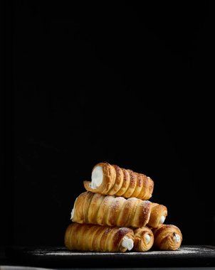 Siyah ahşap bir mutfak tahtasının üzerinde çırpılmış yumurta beyazıyla dolu fırında tüpler.