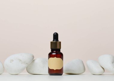 Üzerinde kağıt etiket ve taşların ortasında beyaz bir masanın üzerinde pipet olan kahverengi bir cam şişe. Kozmetik, yağ ve esanslar için kaplar