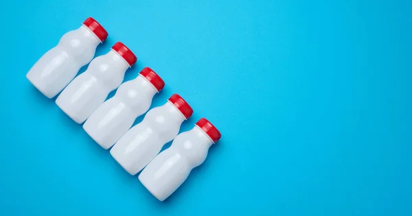White plastic bottles with red caps for dairy products on a blue background, top view
