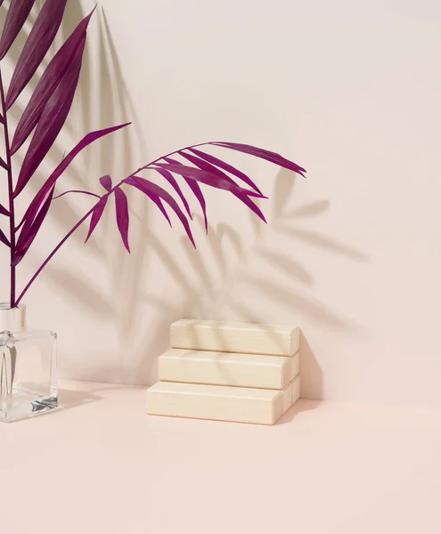 Wooden steps for the display of cosmetics and a purple palm leaf on a beige background. Stage for advertising and product promotion