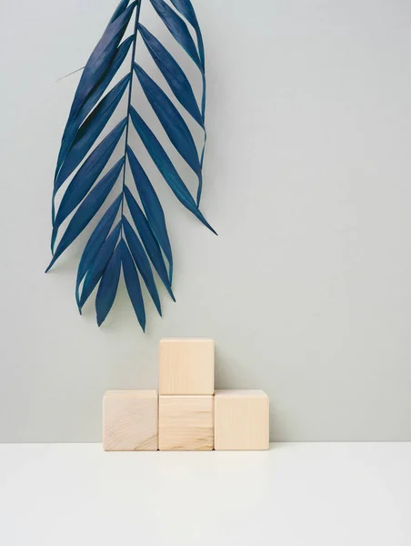Wooden cube on a gray background with a blue palm leaf. Stage for product demonstration, cosmetics. Promotion and advertising
