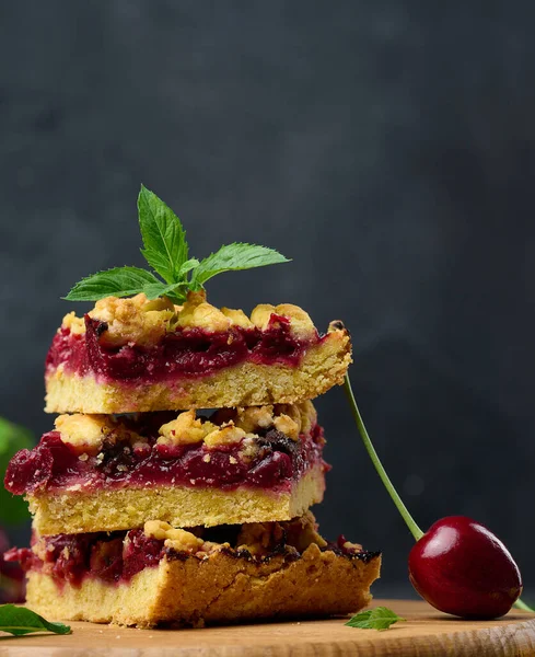 stock image Square slices of cherry crumble lie in a stack on a black background, summer dessert