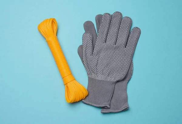 A pair of gray textile protective work gloves and an orange rope on a blue background, top view