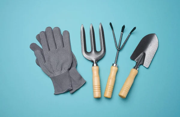 Garden tools for processing beds in the garden and textile gloves on a blue background, top view