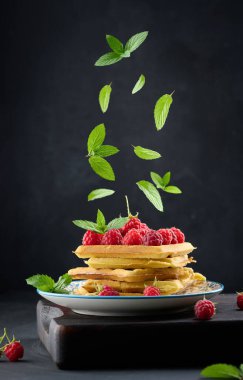 Olgun kırmızı ahududu ve yukarıdan düşen yeşil nane yapraklı fırında Belçika waffle 'ları.