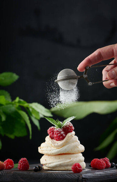 Baked cake made from whipped chicken protein and cream, decorated with fresh berrie. A woman's hand holds a sieve with powdered sugar and sprinkles a dessert