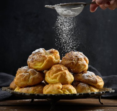 Kremalı krema ile fırınlanmış ekler. metal yuvarlak bir tabakta üzerine şeker serpiştirilmiş.