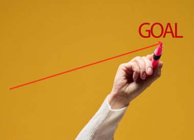 Bir el sarı arka planda kırmızı işaretli bir çizelge çizer. Hedeflerin başarıları