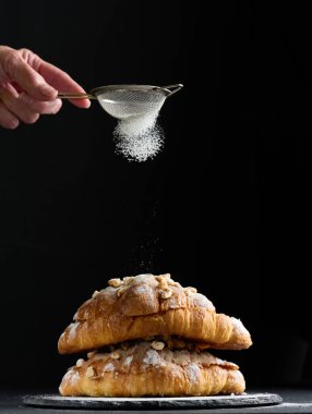 Kurutulmuş kruvasan ve üzerine pudra şekeri serpiştirilmiş, siyah masa. Kahvaltı için iştah açıcı hamur işleri.
