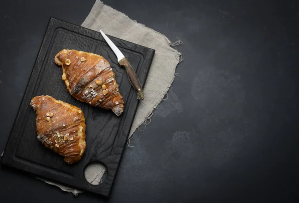 Baked croissant on a  board and sprinkled with powdered sugar, black table. Appetizing pastries for breakfast