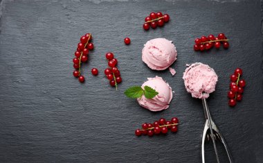 Siyah bir taş tahtada pembe dondurma topları, yakınlarda kırmızı frenk üzümü, üst manzara.