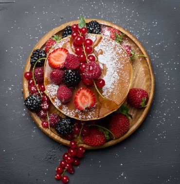 Siyah arka planda şerbetli taze meyveli krep yığını.