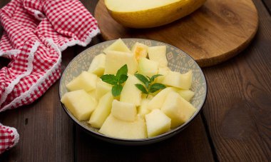 Masanın üzerinde yuvarlak gri bir tabakta dilimlenmiş kavun parçaları.