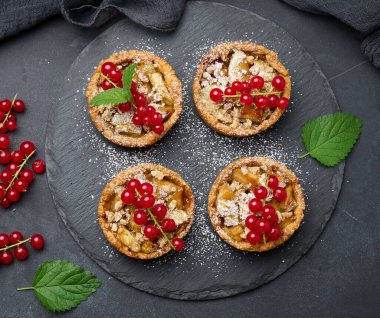 Kırmızı frenk üzümlü meyveli tart üzerine pudra şekeri serpiştirilmiş siyah masa, lezzetli tatlı.