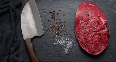 Çiğ sığır filetosu tahtada, siyah masada yatıyor. Yukarıdan görüntüle