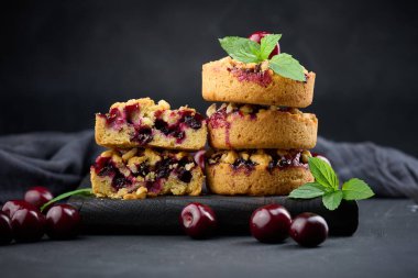 Yeşil nane yaprakları ve siyah arka planla süslenmiş, kirazlı porsiyon parçacıklı turta.