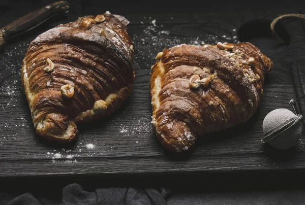 Baked croissant on a  board and sprinkled with powdered sugar, black table. Appetizing pastries for breakfast