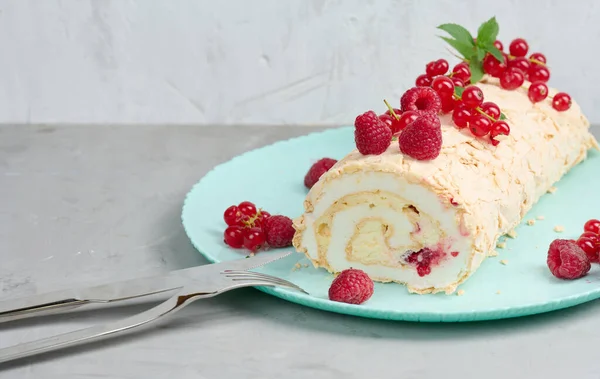 Baked meringue roll with red berries on a round plate, white background