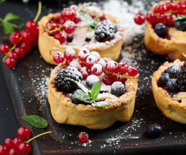 Fruit tart with red currants sprinkled with powdered sugar on a black table