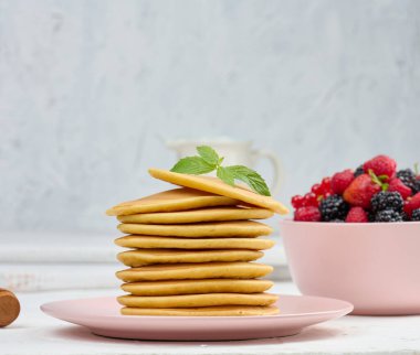 Beyaz bir masada yuvarlak bir tabakta meyveli krep yığını.
