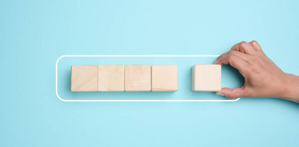 A woman's hand holds wooden cubes on a blue background. The concept of loading the process, the beginning of new achievements