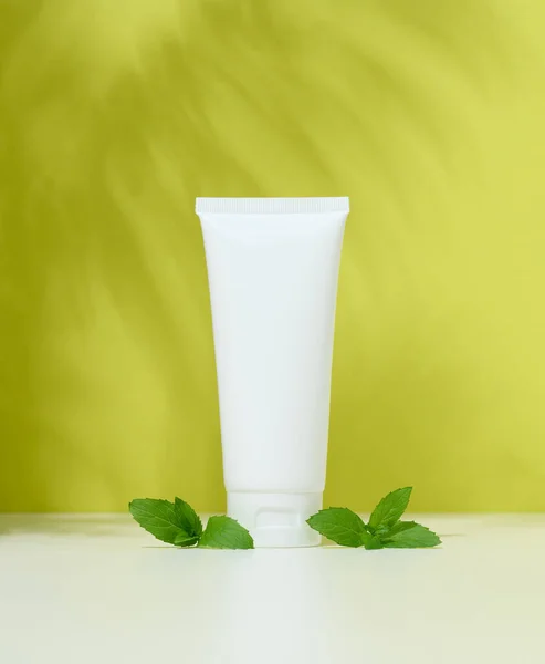 Empty white plastic tubes for cosmetics on a green background. Packaging for cream, gel, serum, advertising and product promotion