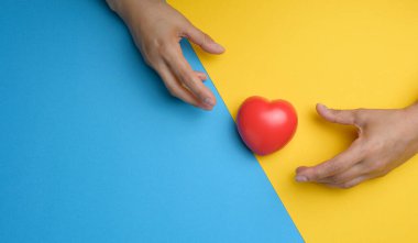 Red heart and stretching hands towards it on a yellow blue background. The concept of helping, kindness and compassion