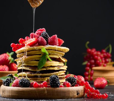 Siyah arka planda bal serpiştirilmiş taze meyveli krep yığını