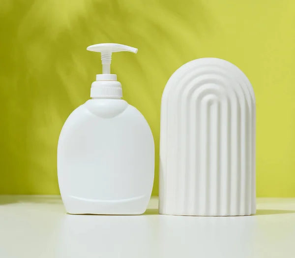 White plastic container with a pump for cosmetic liquid, liquid soap on the table. Green background