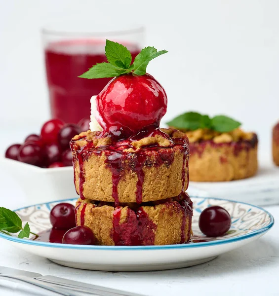 Bir kepçe dondurmayla süslenmiş vişneli turta ve üzerine kiraz sosu serpiştirilmiş.